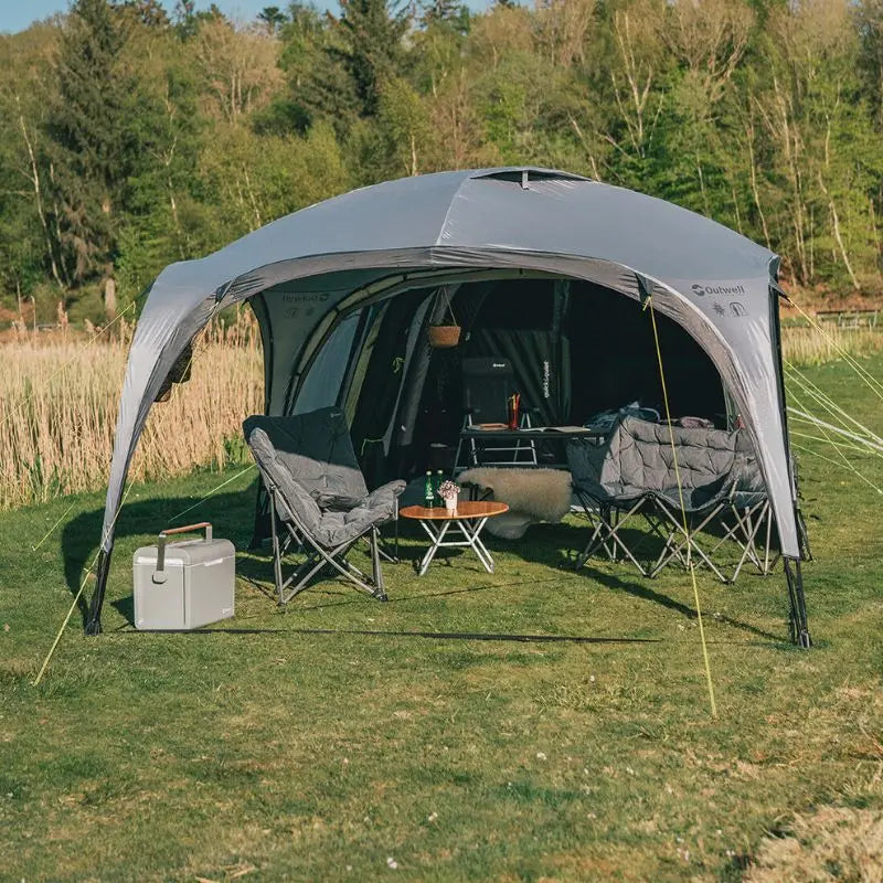 Outwell Event Lounge with furniture and equipment set up in a grassy area with trees in the background.
