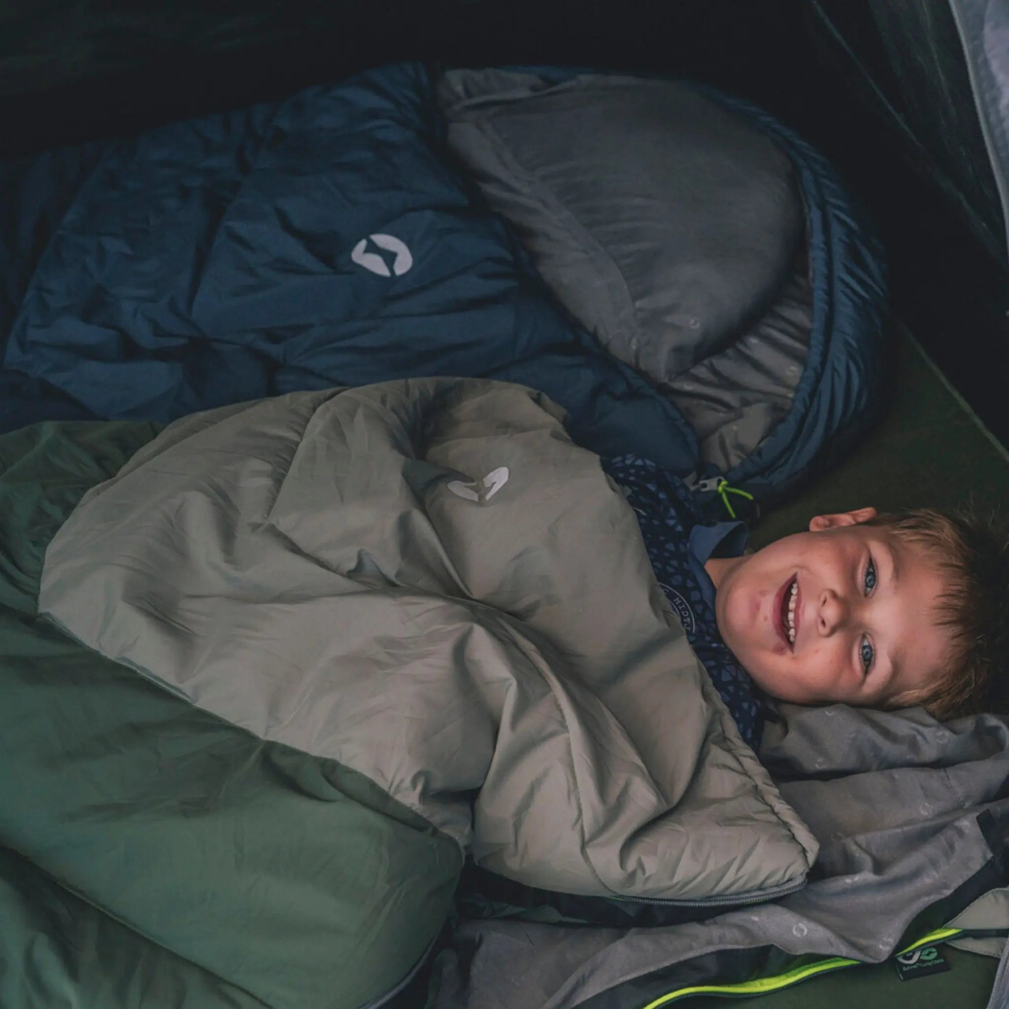 Child wrapped in a cosy sleeping bag inside a tent, designed for camping comfort.