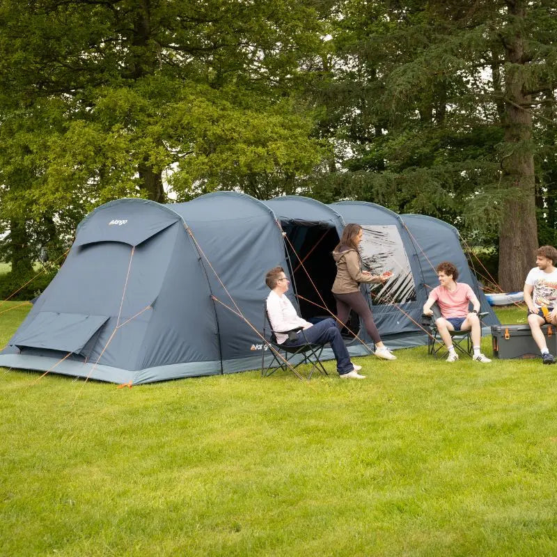 People sitting outside a large 8 person camping tent in a grassy area with trees.