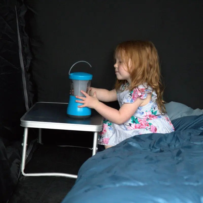Child playing with a blue lantern on a small table inside a darkened tent bedroom.