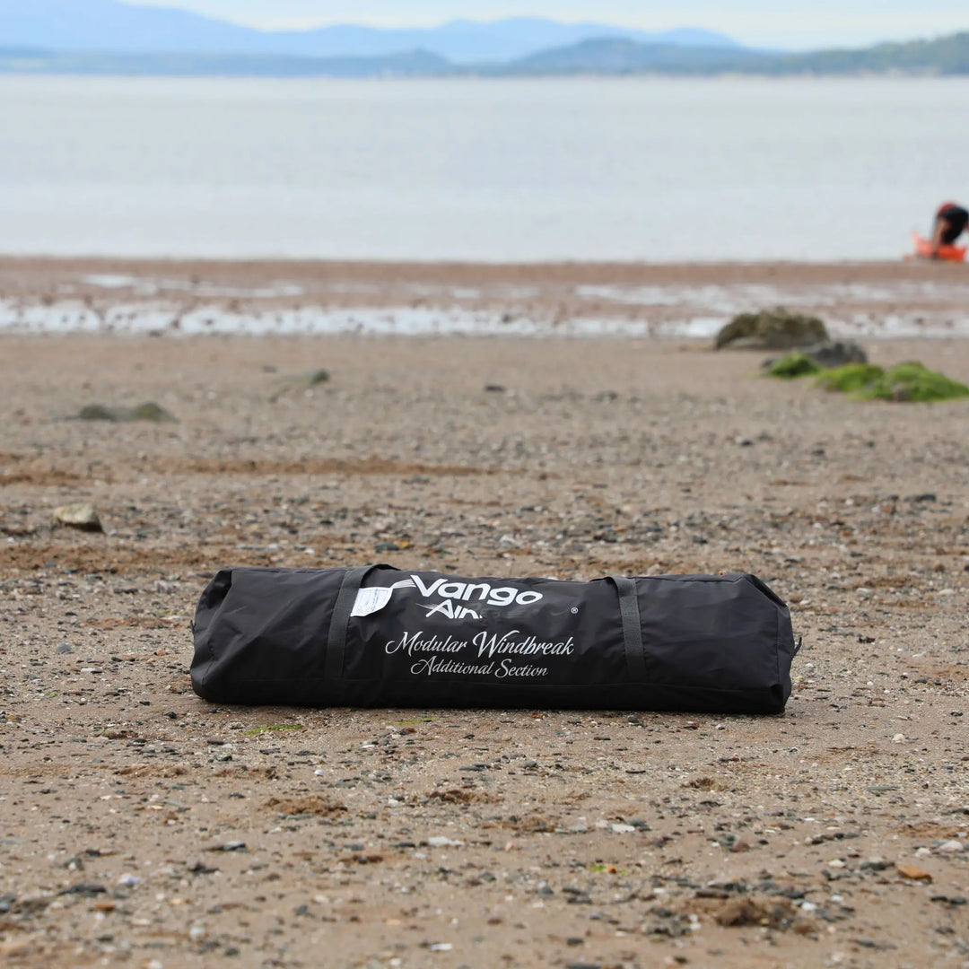 Vango AirBeam Modular Windbreak packed away in its carry bag on a beach with mountains in the background