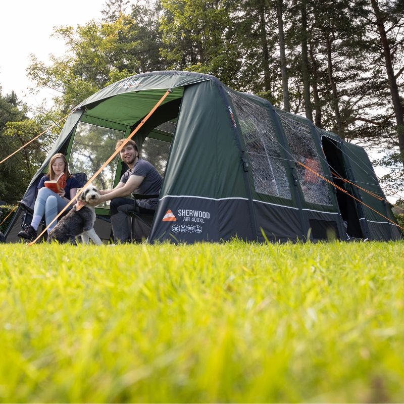 A couple with a dog sitting outside the Vango Sherwood Air 400XL tent, highlighting its green exterior, large windows, and spacious design for family camping.