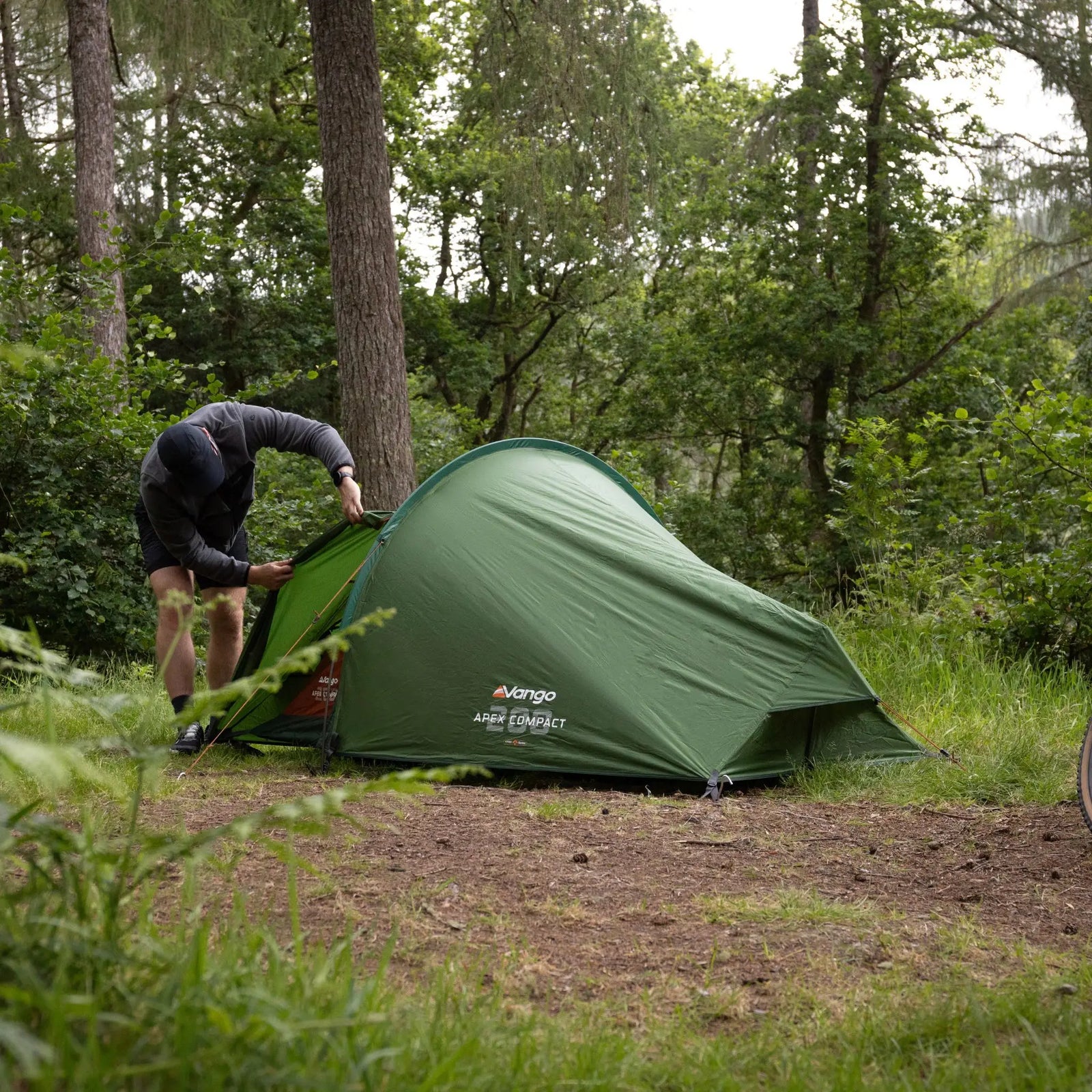 A camper pitching the Vango Apex Compact 200 Tent in the woods. Compact and lightweight design for backpacking trips.