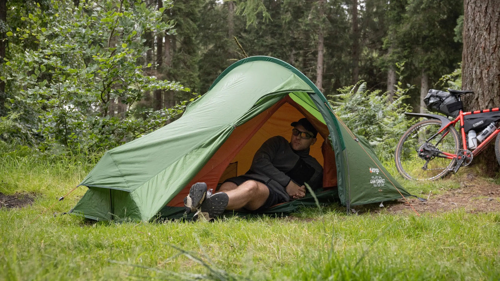 Lifestyle image of a person relaxing in the Vango Apex Compact 200 Tent, surrounded by greenery. A compact 2 man tent for trekking and backpacking.