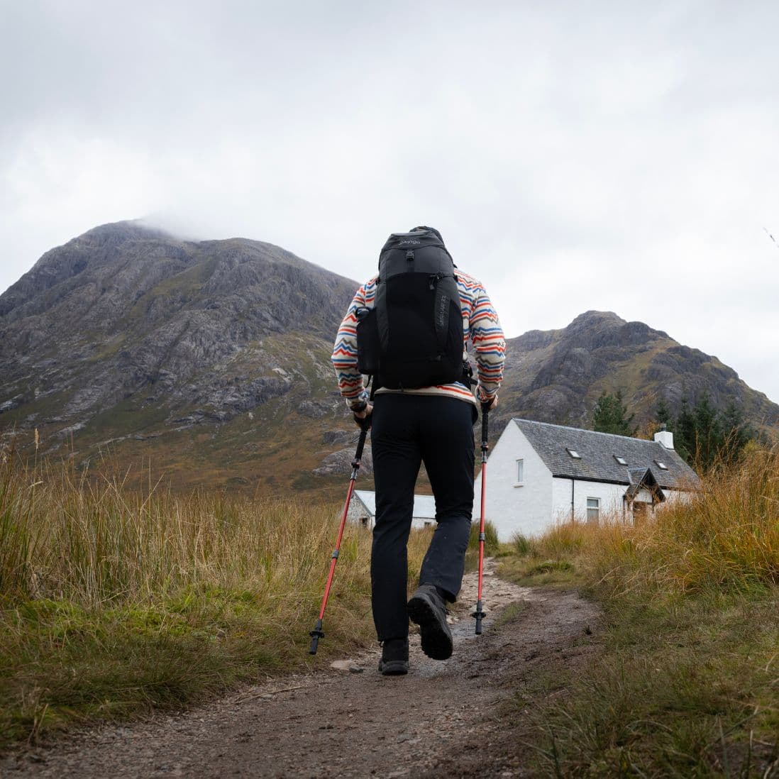 Rear view of a hiker walking along a trail with the Vango Basho Folding Walking Poles, emphasizing their portability and outdoor use.