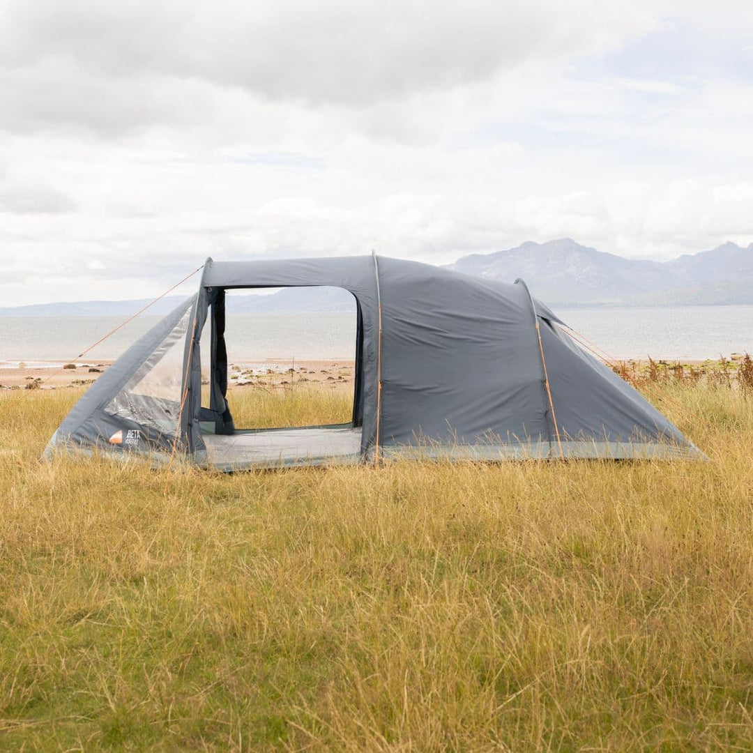 Side view of the Vango Beta 450XL tent pitched in a grassy field, highlighting the open side door and spacious interior with coastal scenery in the background.