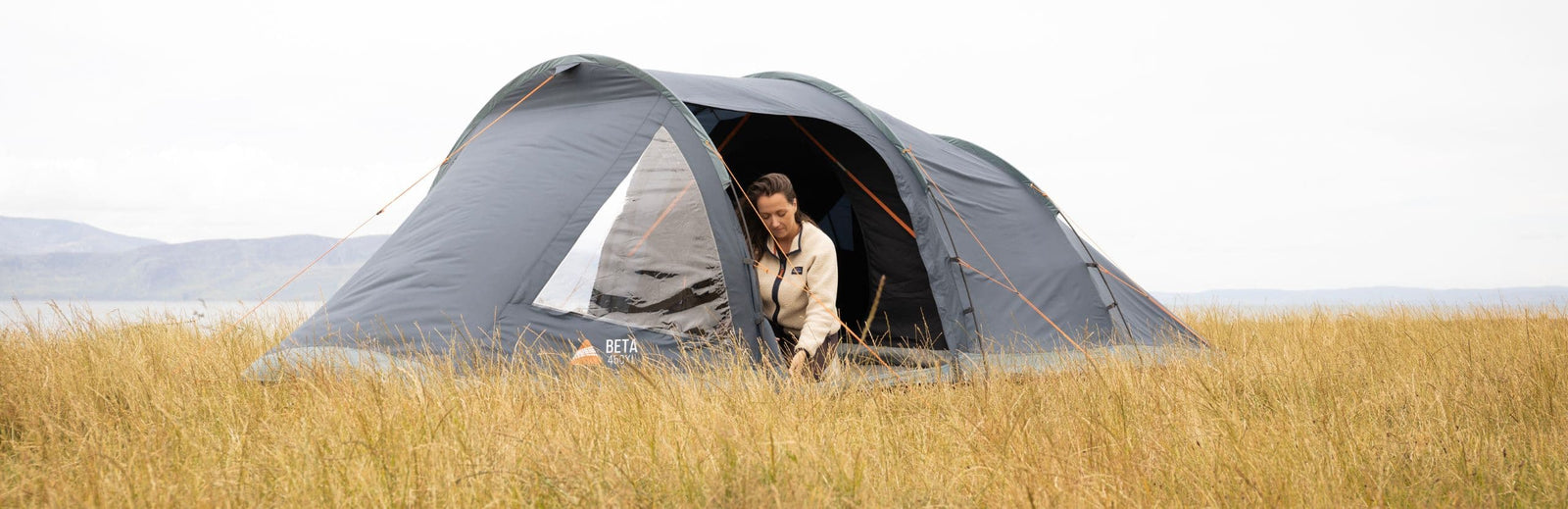 Vango Beta 450XL tent pitched in a scenic grass field with a woman using the front entrance.