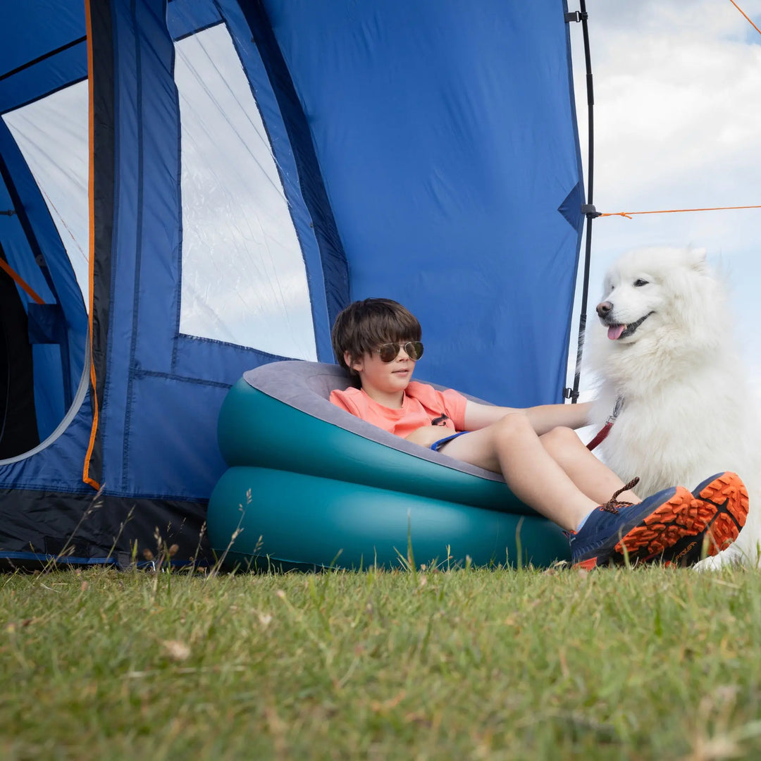 Child sitting on an inflatable chair next to a dog in front of a Vango Capri 400 Tent.
