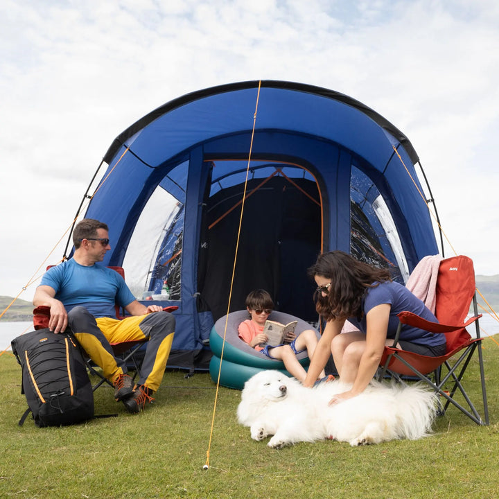 Family with a dog sitting outside a Vango Capri 400 Tent on a grassy area.