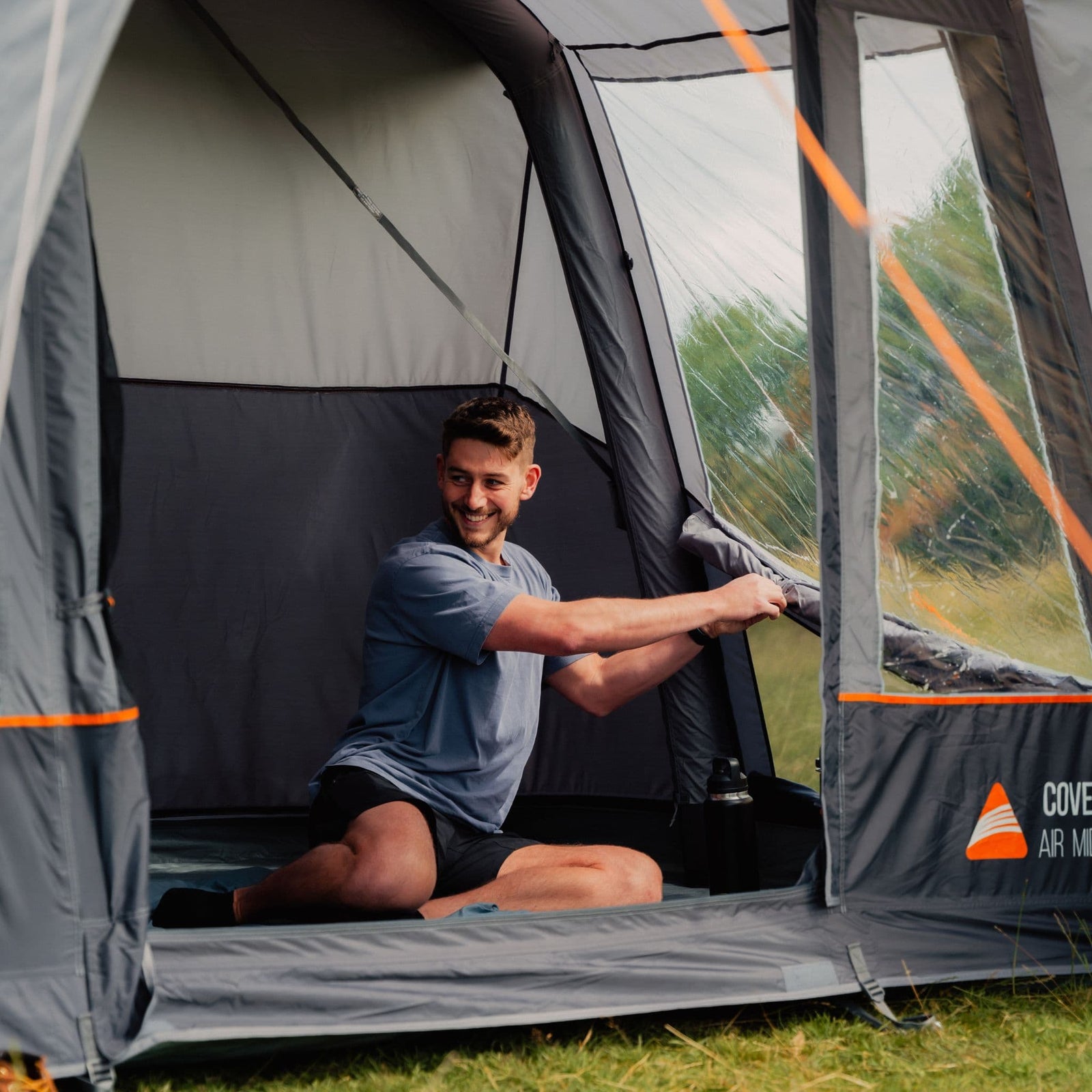 Interior view of the Vango Cove III Air Awning with a man rolling up the window panels, highlighting its versatile design for ventilation and natural light.