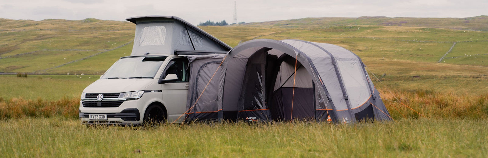 VW campervan with the Vango Cove III Air Low Drive Away Awning setup in a scenic grassy field, showcasing extra living space and compact design for campervan trips.