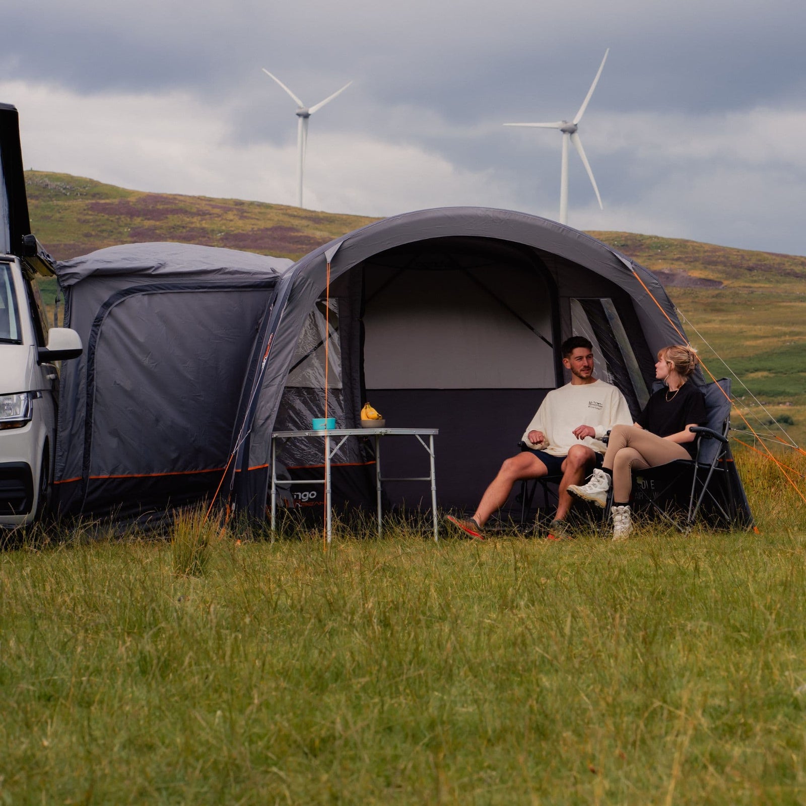 Vango Cove III Air Low Drive Away Awning attached to a VW campervan, set in a scenic location with two people enjoying the extra living space provided by this campervan awning.