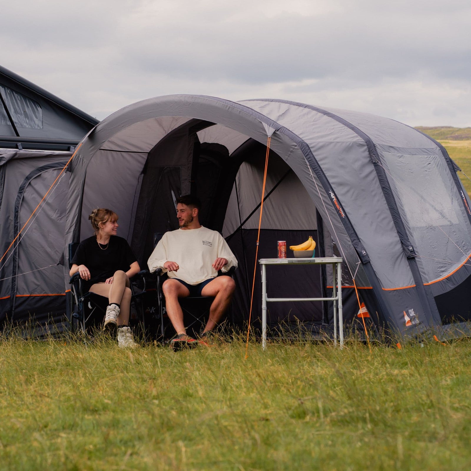 Front view of the Vango Cove III Air Low Drive Away Awning attached to a VW campervan, with two people relaxing and showcasing the awning's spacious interior and sturdy design.