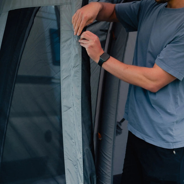 Man securing the entrance door of the Vango Cove III Air Low Drive Away Awning, demonstrating its reinforced zips.