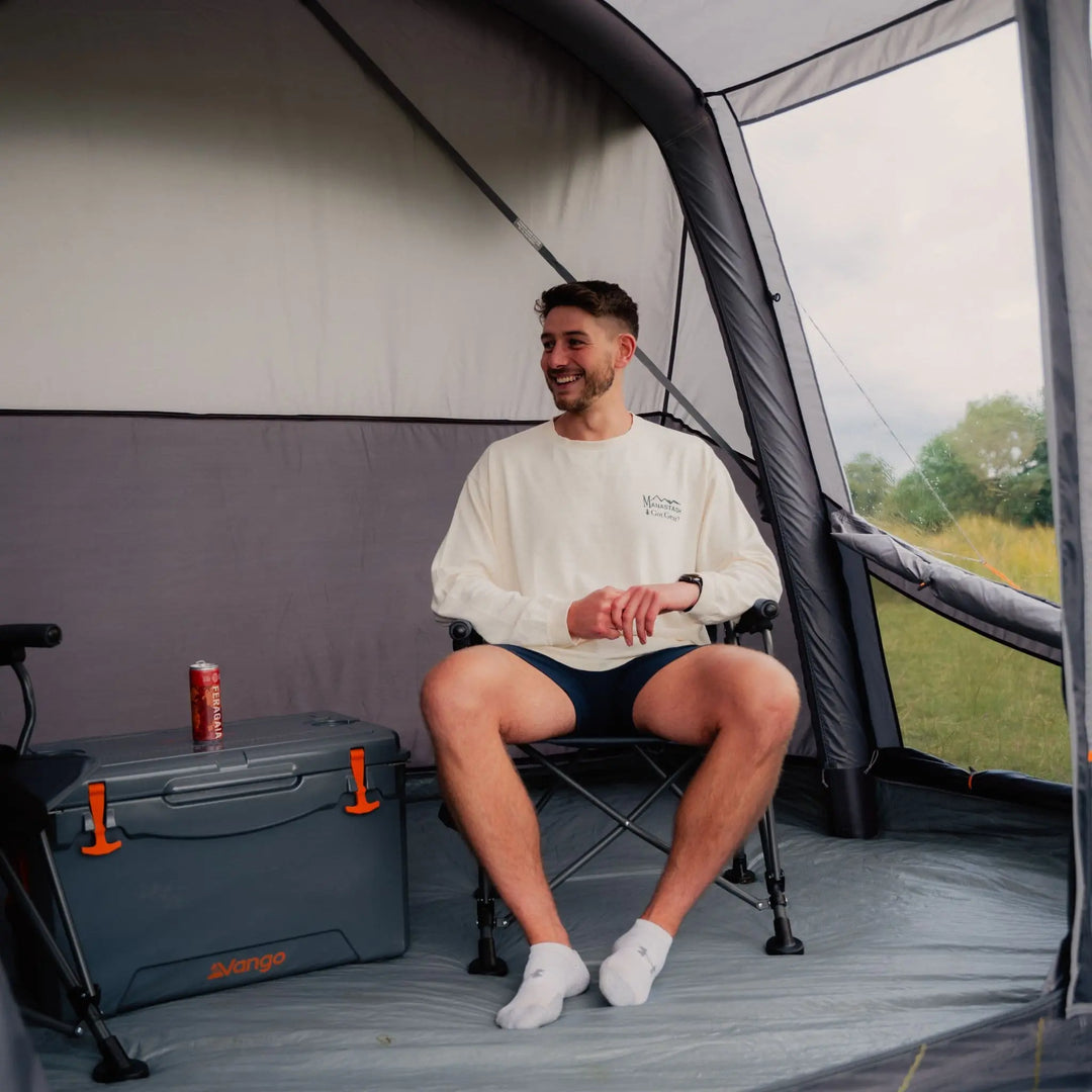 Man sitting comfortably inside the Vango Cove III Air Low Awning, highlighting its ample space for seating and storage during camping trips.