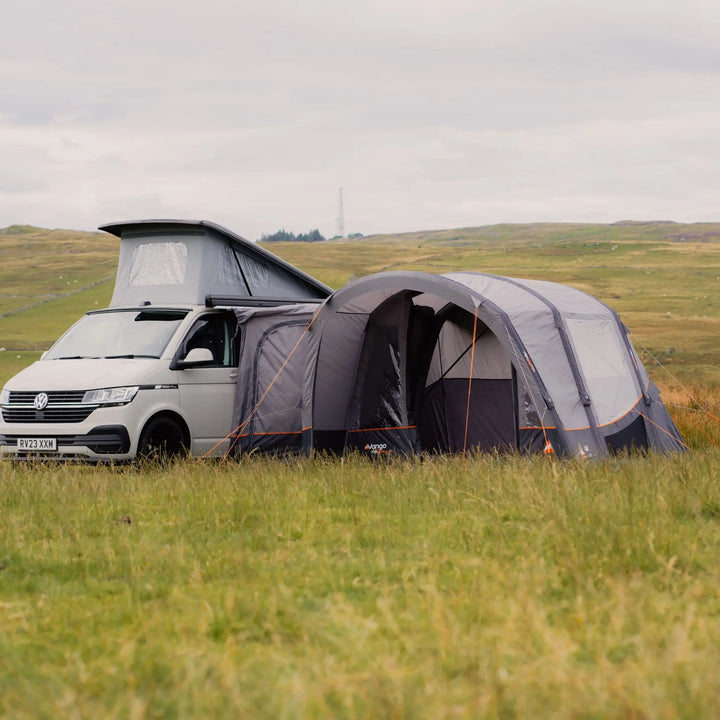 Vango Cove III Air Low Awning attached to a campervan, pitched in a grassy field with the awning fully pitched.