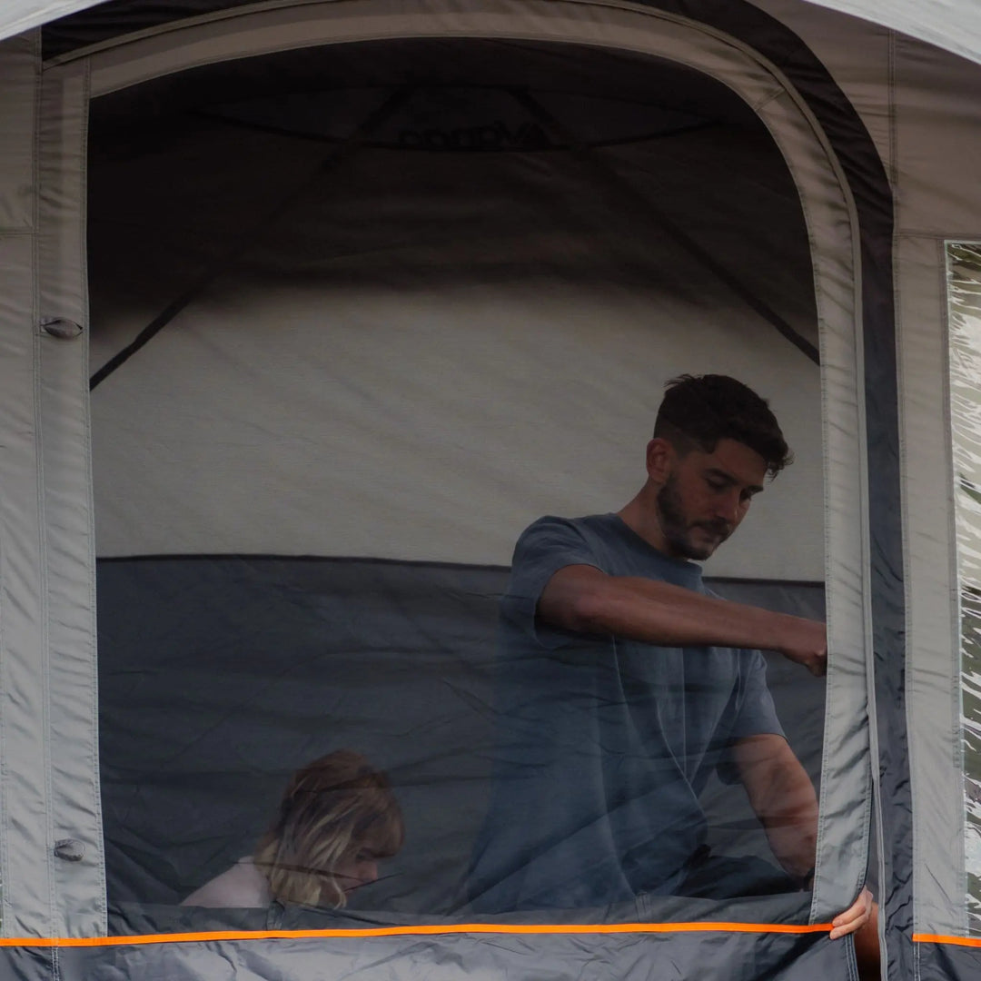 Family visible through the mesh door of the Vango Cove III Air Low Drive Away Awning, showcasing ventilation and insect protection features.