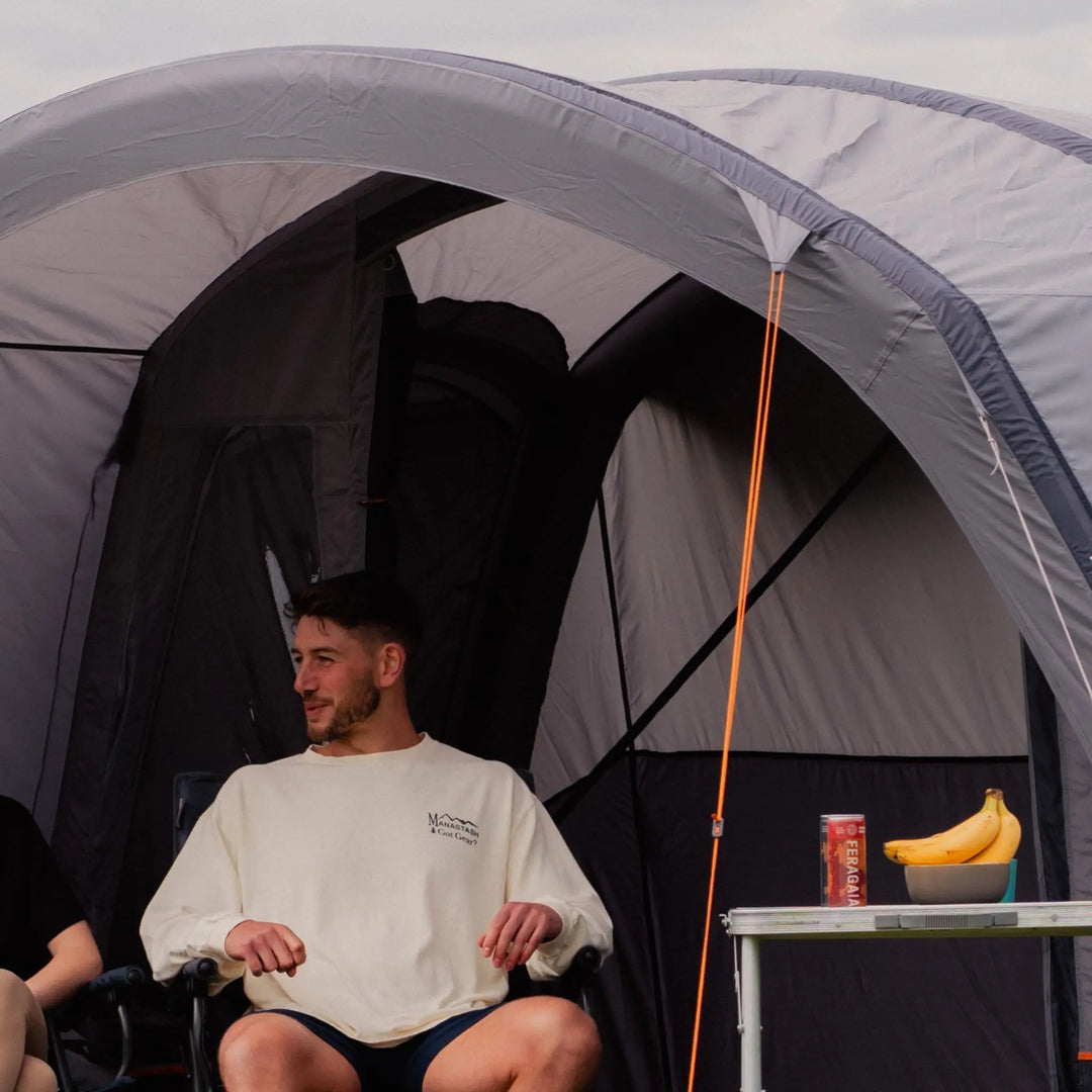 Couple seated outside the Vango Cove III Air Low Drive Away Awning with a table, highlighting its spacious living area and outdoor functionality for camping.