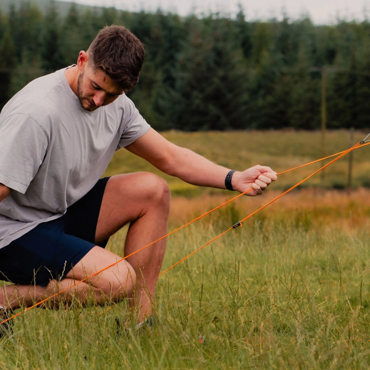 Man securing a guyline of the Vango Cove III Air Low Drive Away Awning in a grassy campsite, demonstrating its stability in outdoor conditions.