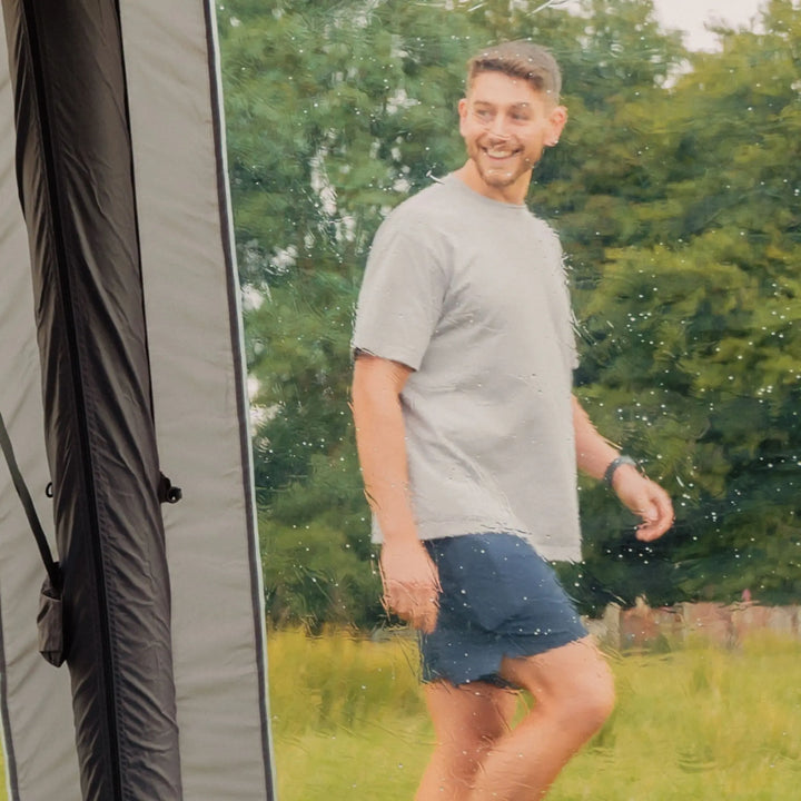 Man walking outside a Vango Cove III Air Low drive-away awning, viewed through the diamond clear window on a rainy day.