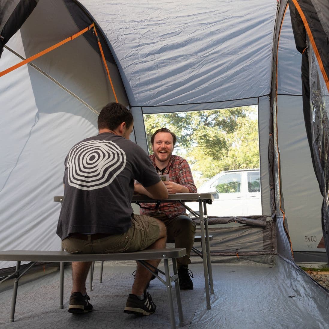 Interior view of the Vango Cove III Low drive away awning, featuring a spacious living area with two people seated at a camping table, ideal for campervan adventures.