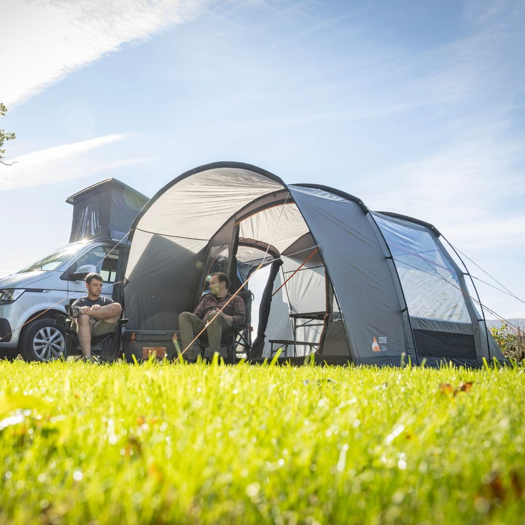 Vango Cove III Low drive away awning pitched beside a VW campervan, showcasing its pre-attached front canopy and clear windows, perfect for outdoor relaxation.