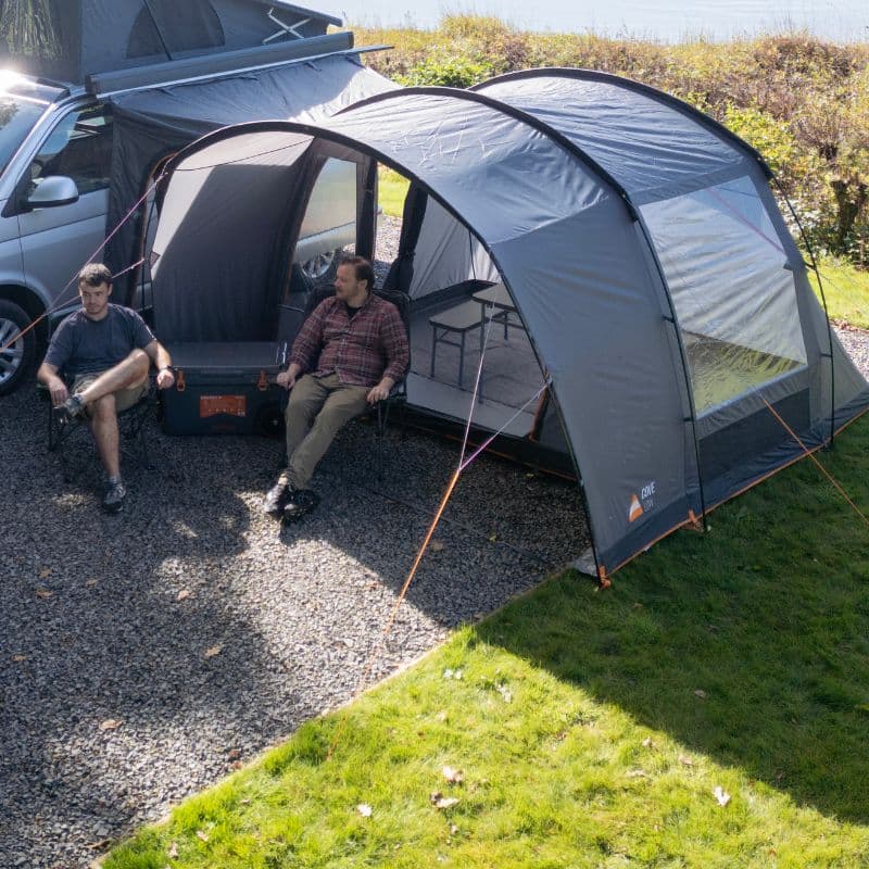 Two men relaxing outside a Vango drive-away awning attached to a campervan, showcasing spacious outdoor living space and connection to the vehicle.