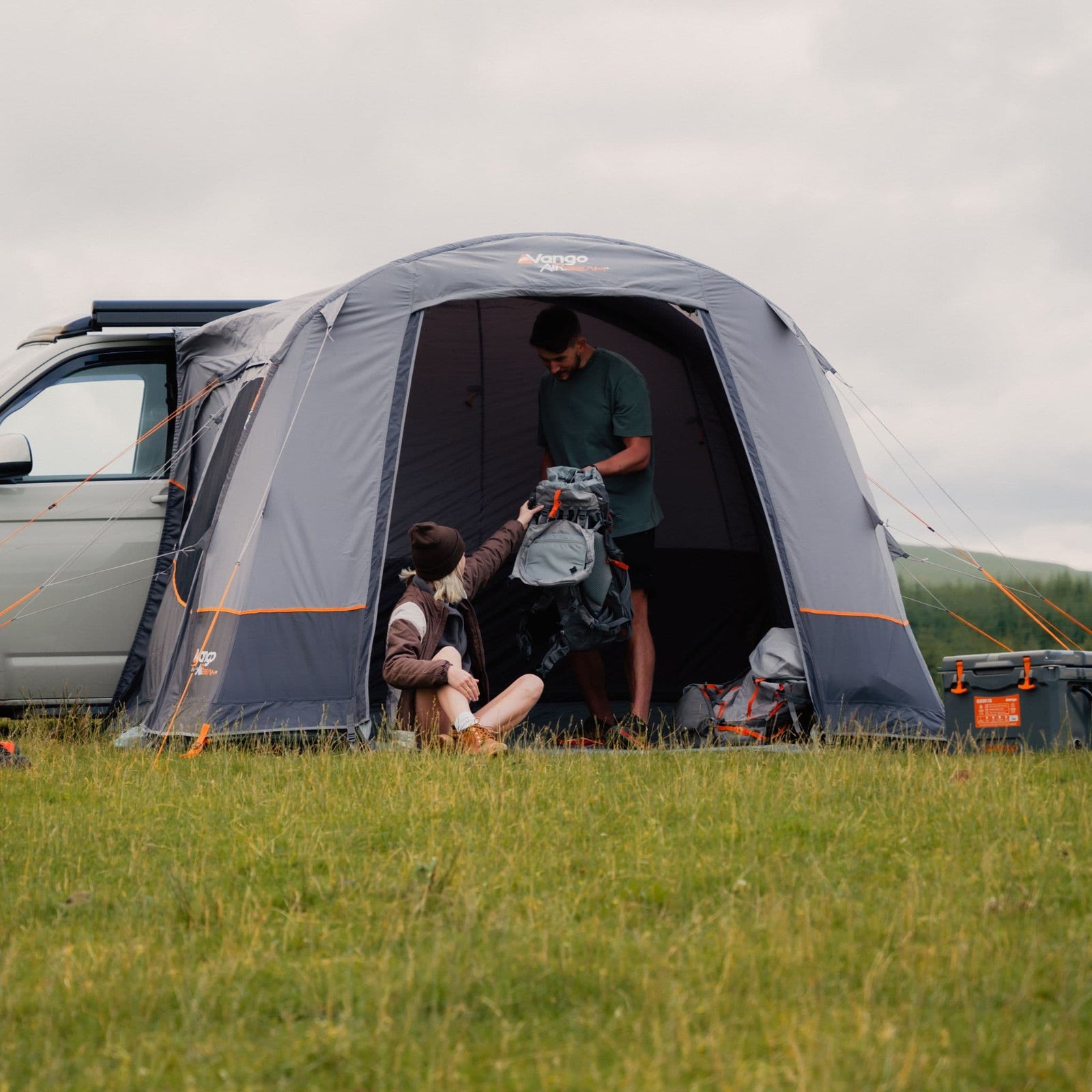 Couple organising gear inside the Vango Faros III Air Low inflatable awning, connected to a VW campervan, showcasing the spacious interior and drive away awning convenience.