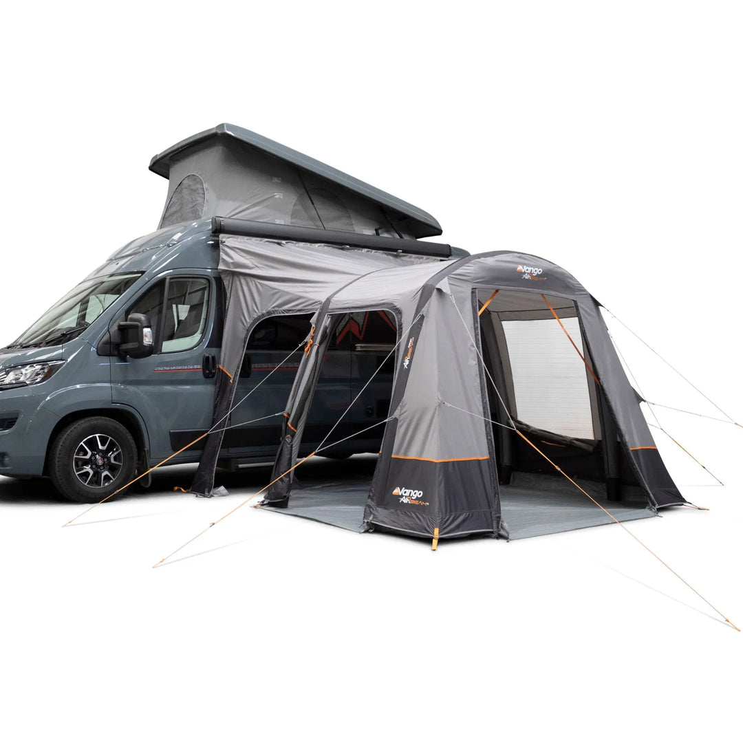 A Vango Faros III Air Mid Drive Away Awning with orange accents attached to the side of a blue-grey van with a raised roof, shown on a clean white background.