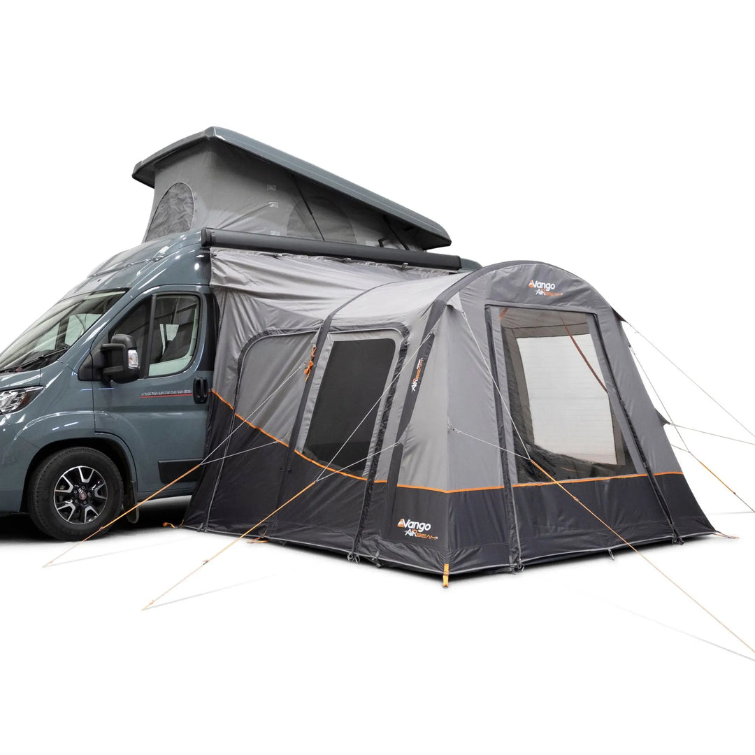 A Vango Faros III Air Mid Drive Away Awning with mesh windows and guy lines, shown attached to the side of a blue-gray motorhome with its pop-up roof raised, on a white background.