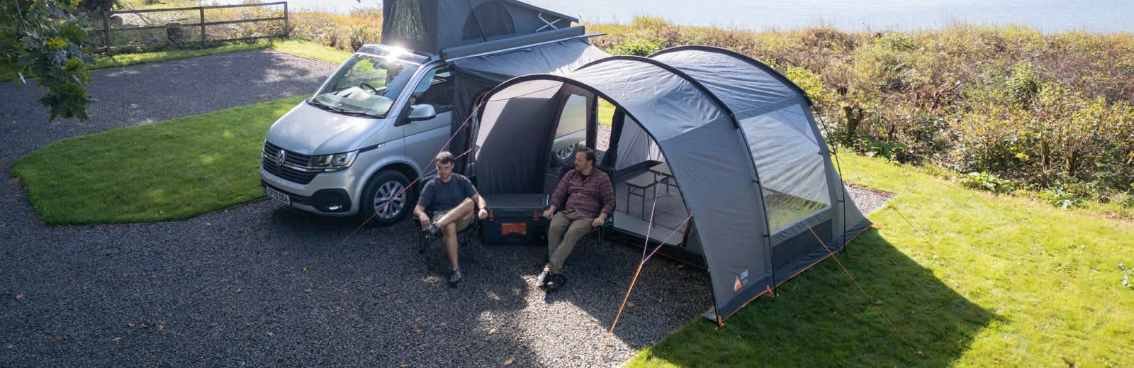 Vango Cove III Low drive away awning pitched beside a VW campervan, showcasing its pre-attached front canopy and clear windows, perfect for outdoor relaxation.