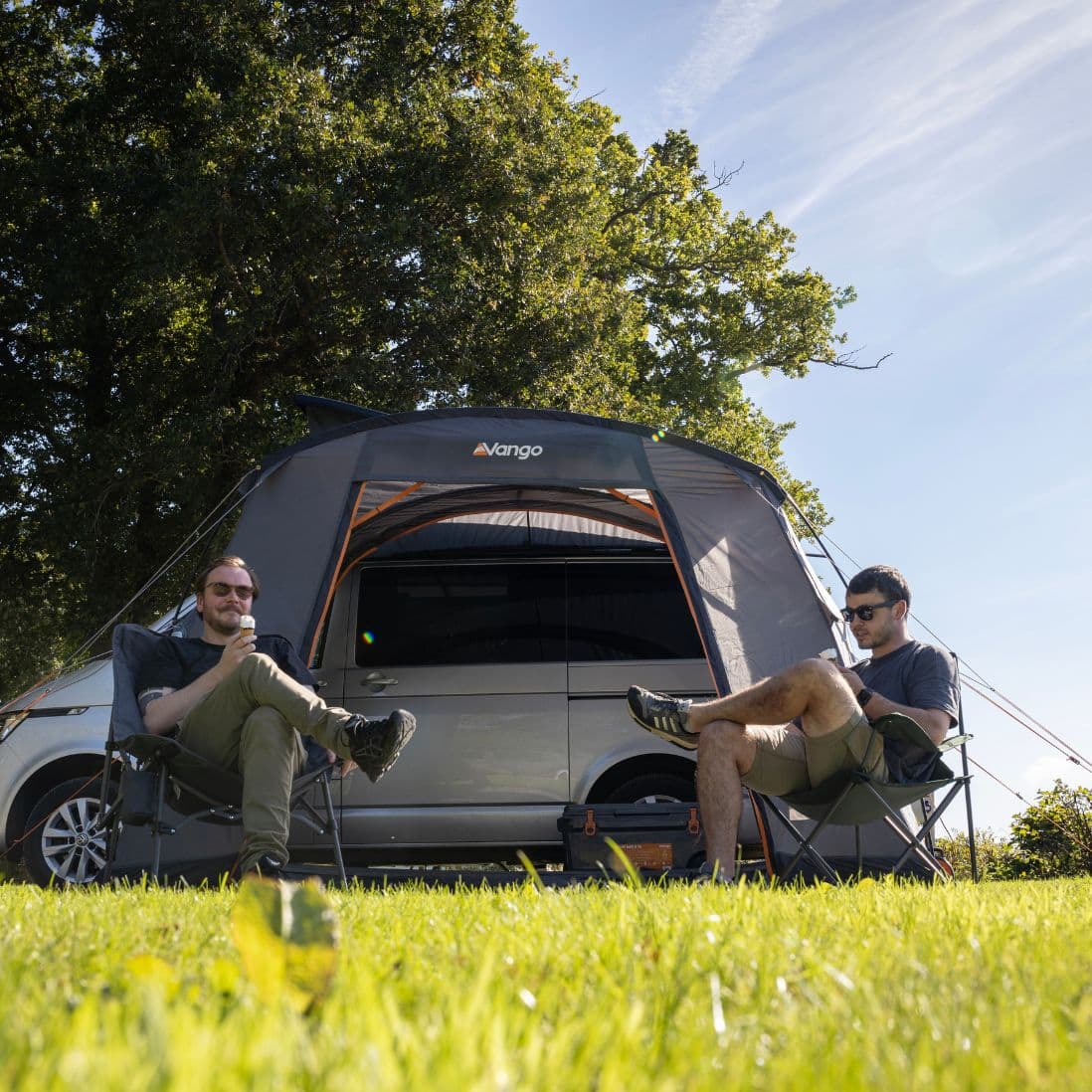 Front view of the Vango Faros III Low Drive Away Awning with two campers enjoying the day, highlighting its practical use with a VW campervan.