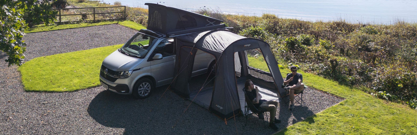 Aerial view of the Vango Faros III Low Drive Away Awning attached to a VW campervan in a scenic camping spot near the water.