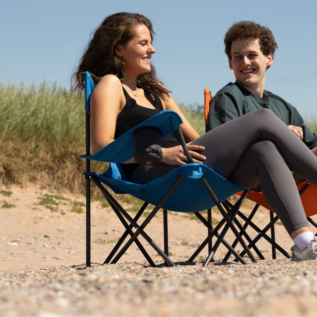 Two people relaxing on the Vango Fiesta Chair and another folding chair on a beach, highlighting its comfort as a portable outdoor chair.