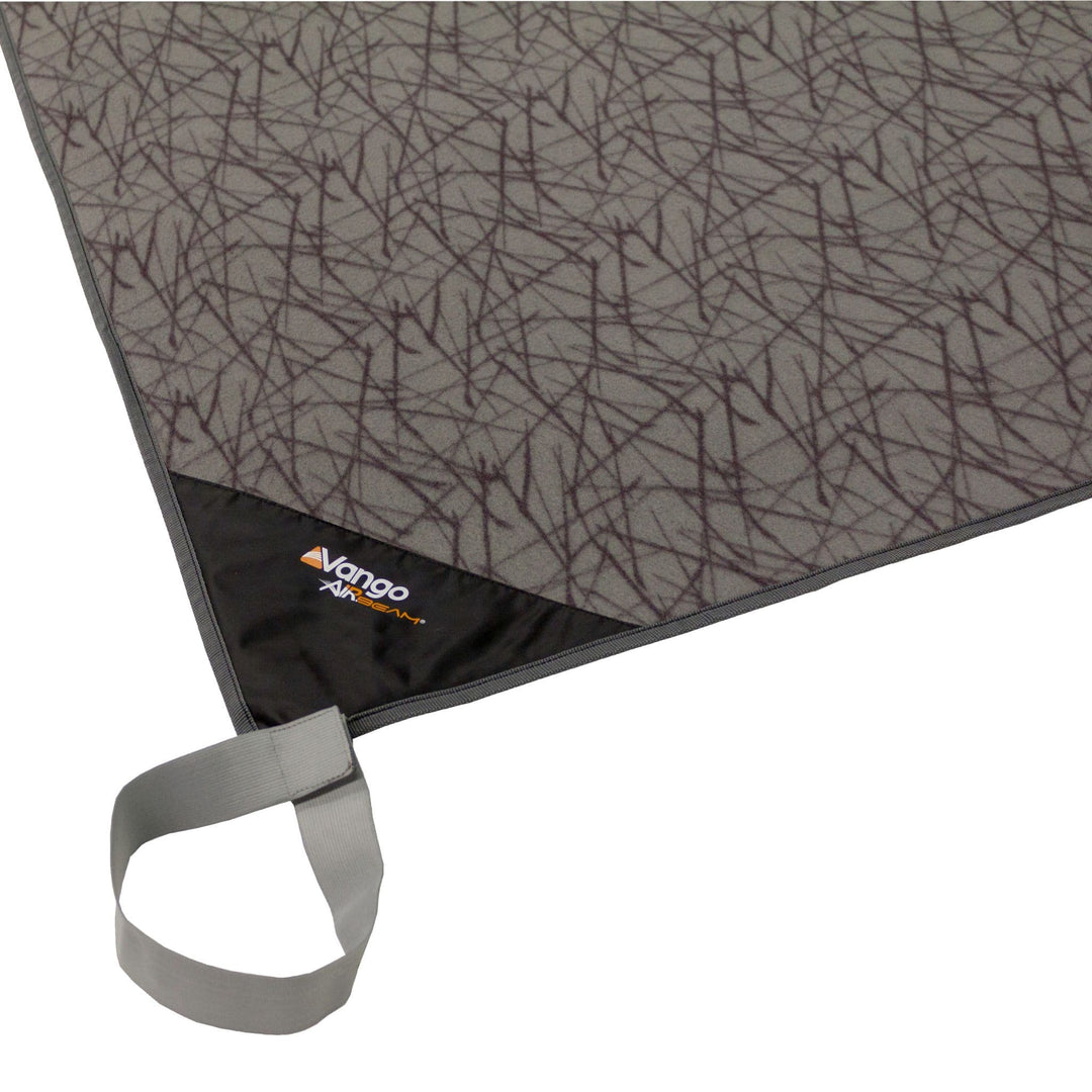 Close-up of the Vango fitted carpet corner, featuring a patterned design with the Vango AirBeam logo and a grey securing strap for a snug fit inside tents.