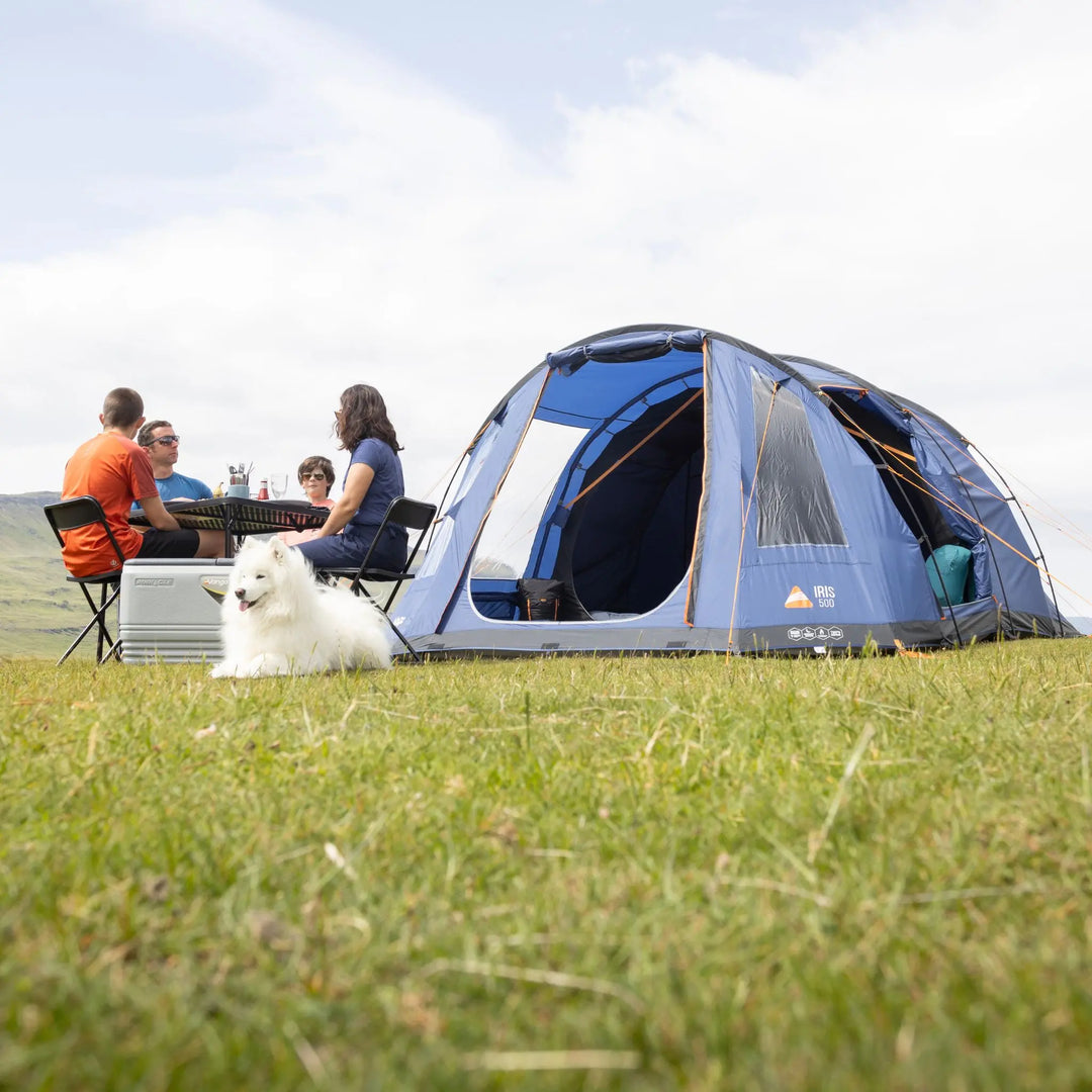 Camping scene with a Vango Iris 500 Tent, people sitting around a table, and a dog on grass.