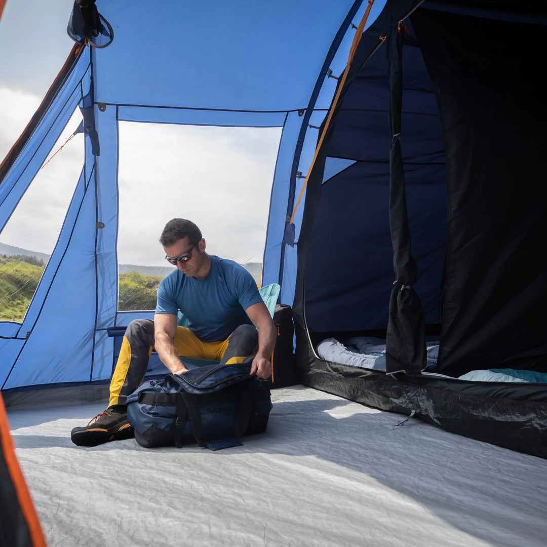Man packing a bag inside a Vango Iris 500 Tent with a scenic background