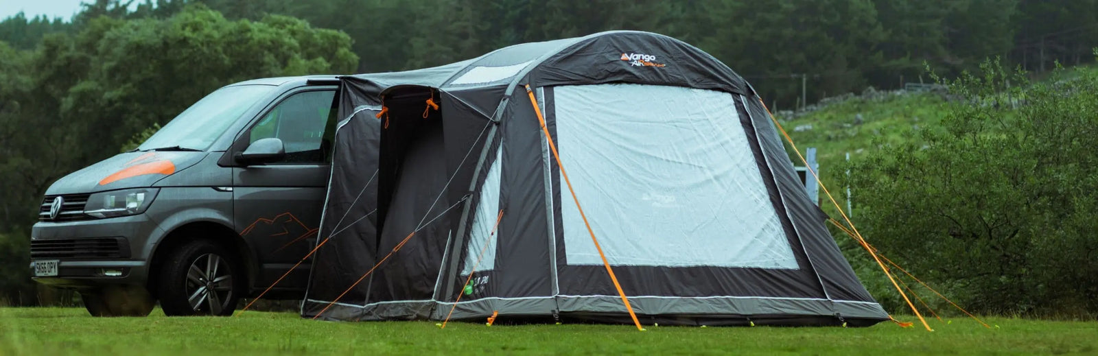 Vango Kela Pro Air Low campervan awning attached to a VW campervan, pitched in a lush green landscape with secured guy ropes.