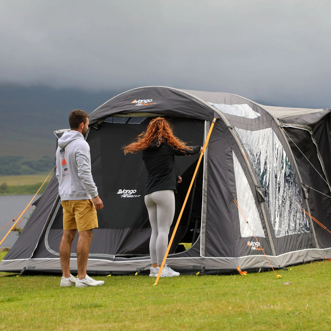 Couple setting up the Vango Kela Pro Air Low campervan awning in a scenic outdoor location with mountains in the background.