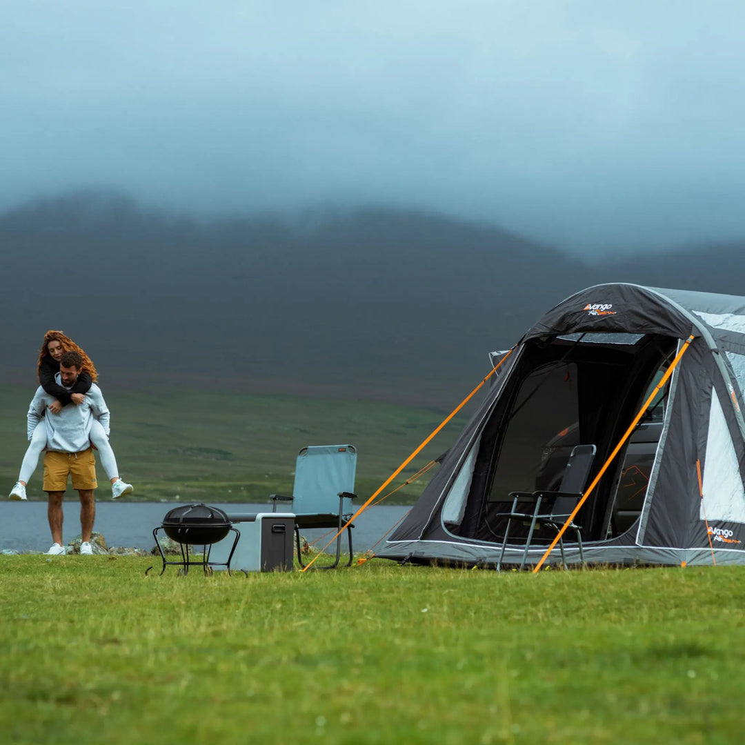 Scenic camping setup with the Vango Kela Pro Air Low drive away awning, campervan, and outdoor furniture beside a misty mountain lake.