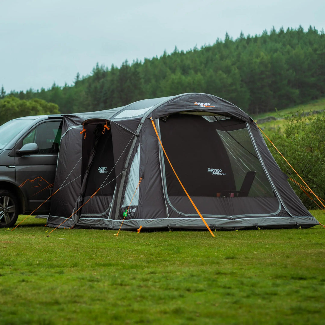 Vango Kela Pro Air Low drive-away awning attached to a VW campervan, pitched in a lush green landscape.