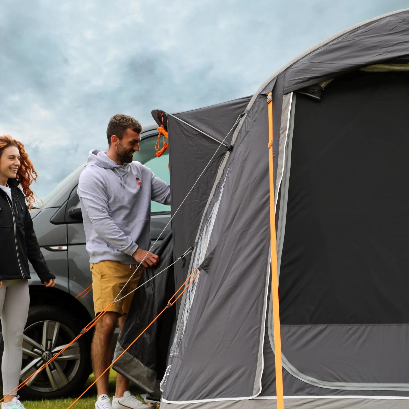 Couple inspecting the side entrance of the Vango Kela Pro Air Low awning, demonstrating its zippered doorway and sturdy structure.