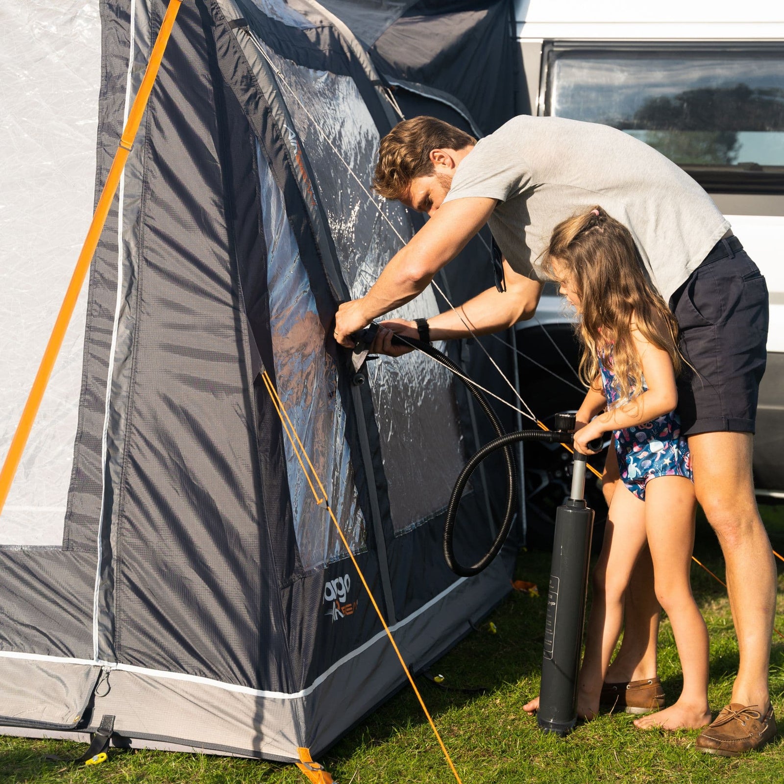 Family inflating the Vango Kela Pro Air Mid Drive Away Awning using the included pump, demonstrating the ease of setup and durable AirBeam technology for mid-height campervans.