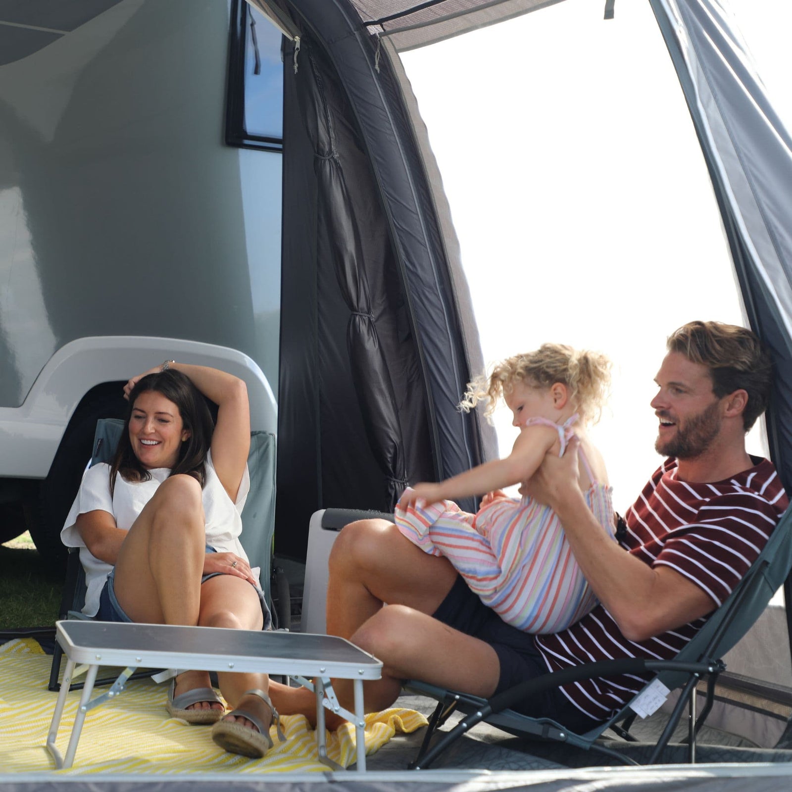 Family enjoying the spacious interior of the Vango Kela Pro Air Tall Drive Away Awning. Highlighting the 6000HH waterproof fabric, Pre-angled Beams for added space, and large windows for natural light.