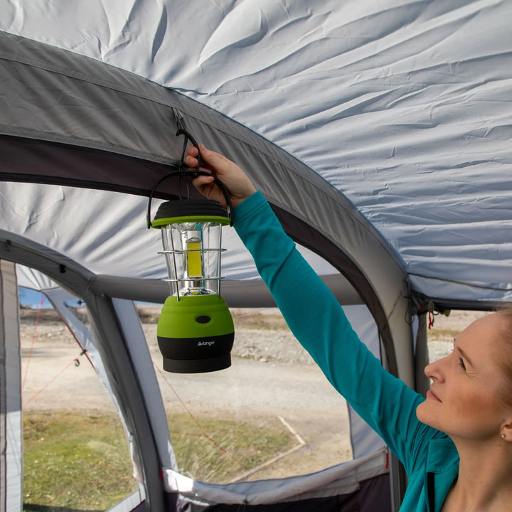 A woman hanging a Vango Lunar 250 ECO Rechargeable Lantern in a tent, showcasing its compact design and green finish, ideal for camping light needs.