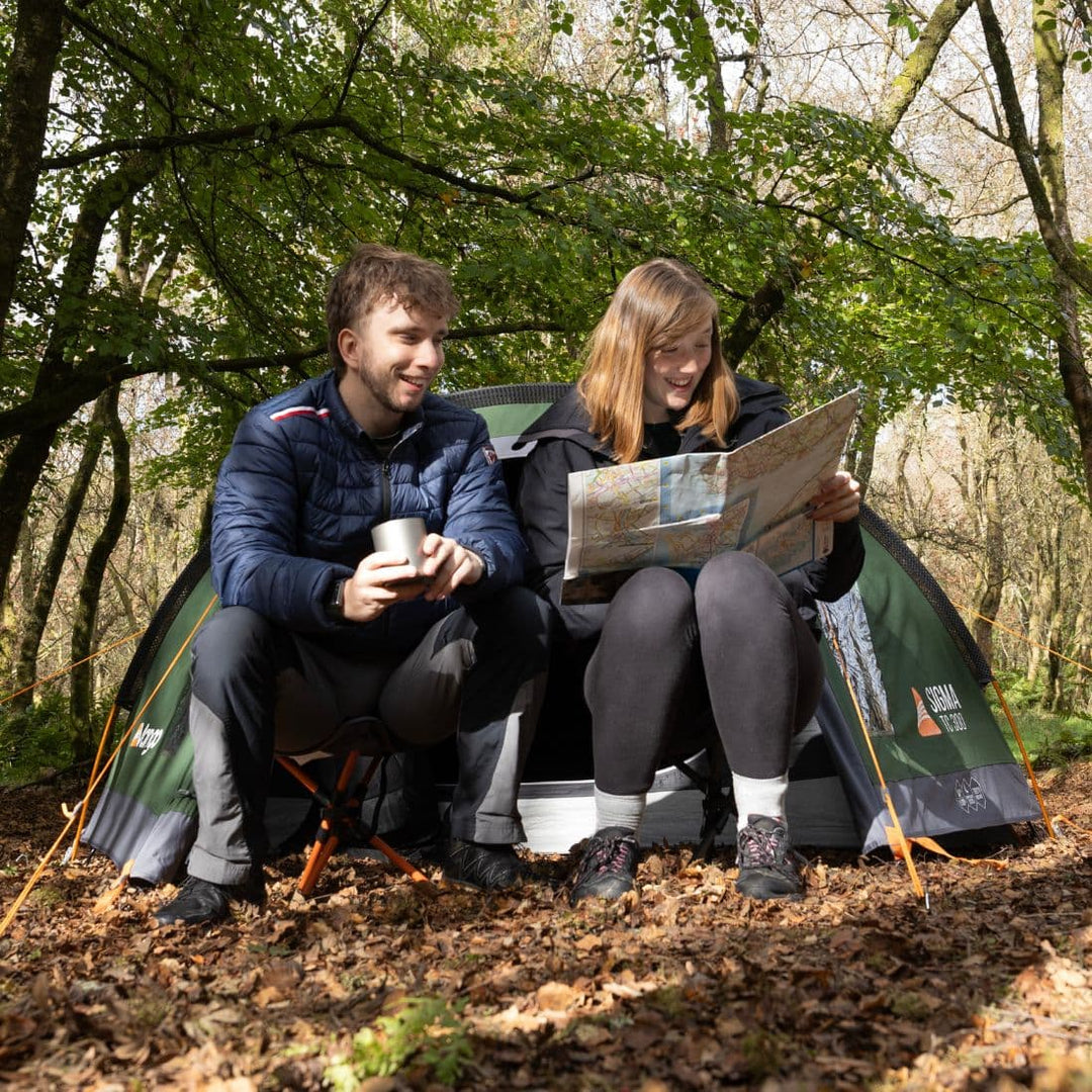 Campers enjoying outdoor relaxation while seated on Vango Micro Stool India Ink – portable, folding camping stool for easy use.