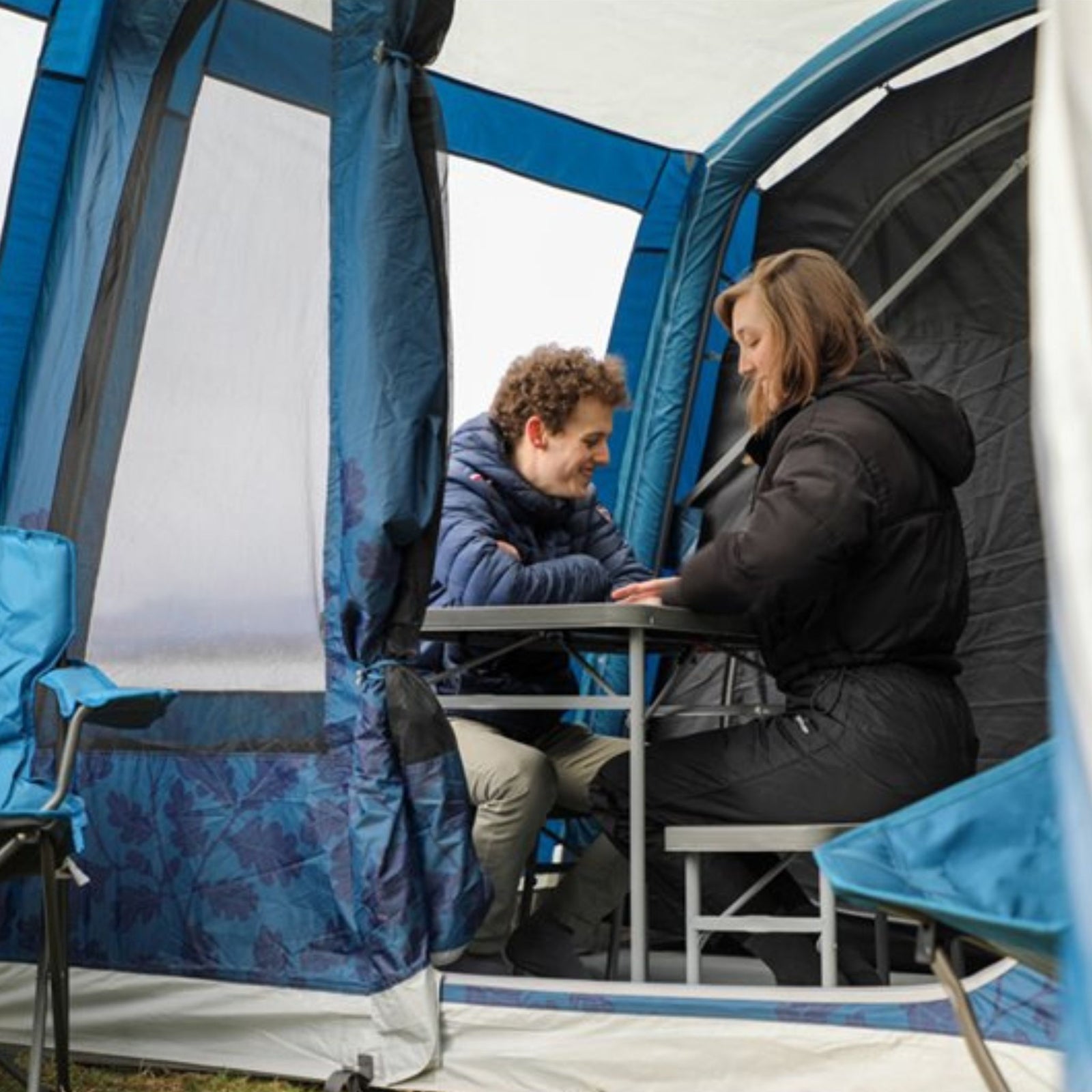 Two people using the Vango Orchard Bench Set inside a camping tent, showcasing its practicality for dining or socialising outdoors.