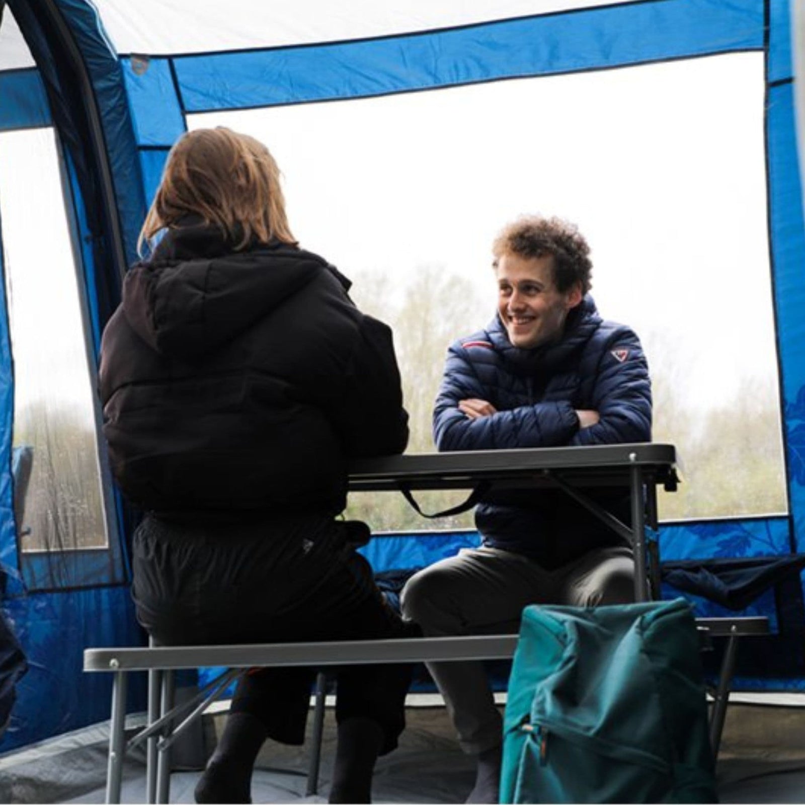 Close-up of a couple sitting at the Vango Orchard Bench Set inside a tent, demonstrating its suitability for camping.