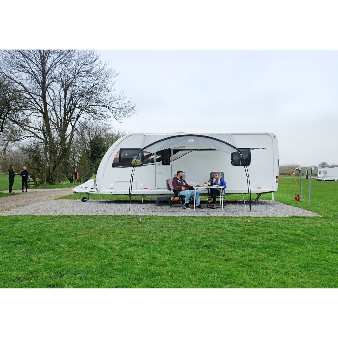 Vango Poled Sun Canopy 3M setup alongside a caravan, providing a comfortable shaded area for outdoor activities.