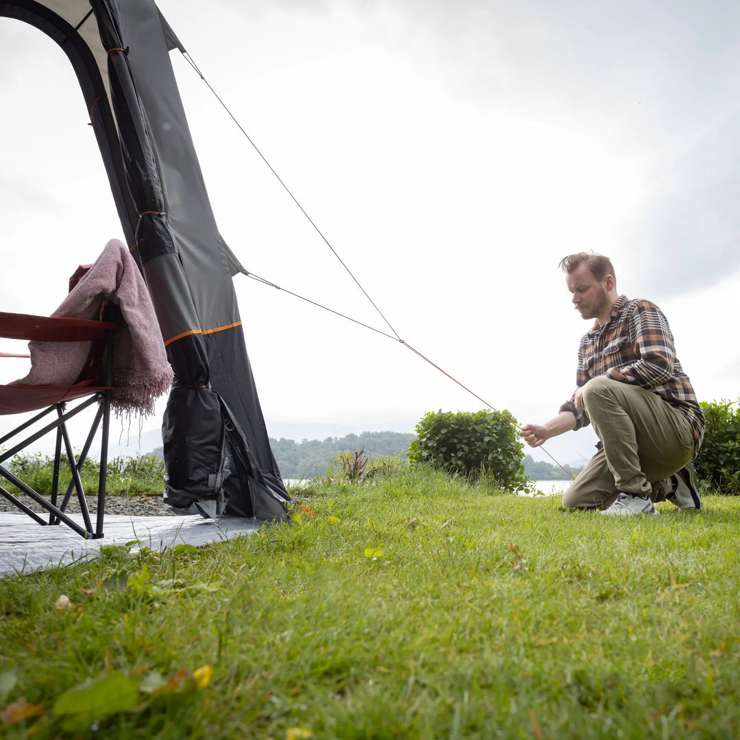 Man pitching a Vango Quadris Air Low Drive Away Awning near a lake with grass and trees in the background.